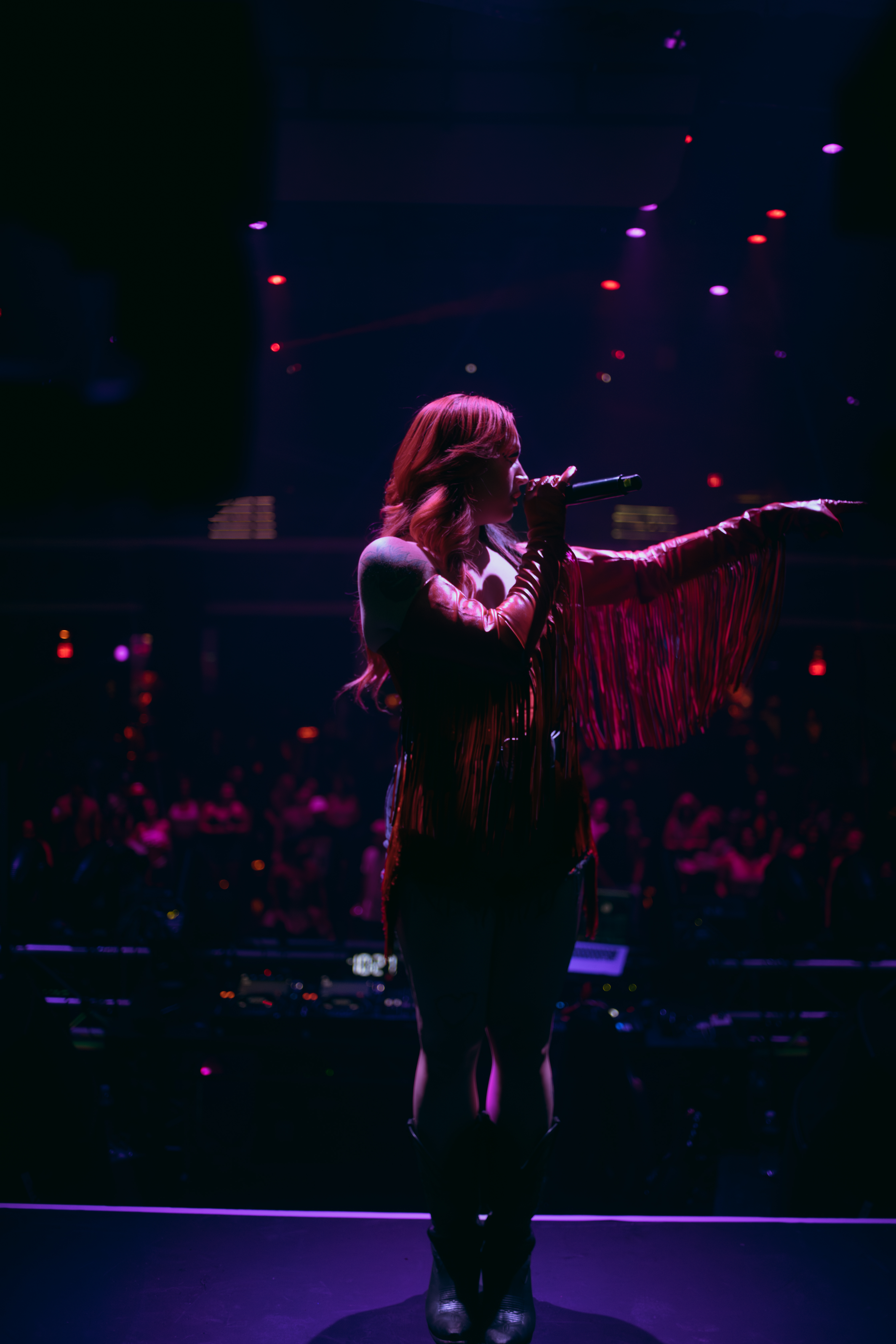 The Redheaded Cowgirl on a festival stage under red and violet light